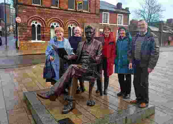 5 people from Book Group 3 standing around a seated statue of Arnold Bennett outside in the street