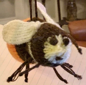 A knitted bee with white wings, orange body and brown legs