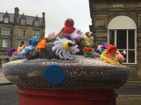 A brown crocheted cover for a postbox with knitted characters on top