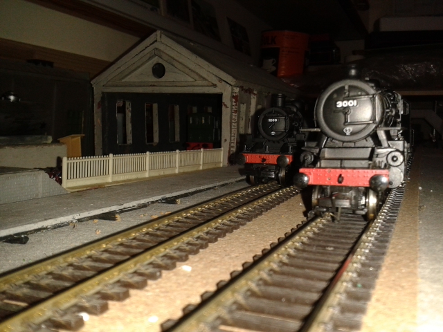 Two black trains on parallel tracks with shed on left of image One train is labelled 3001. The other number is unreadable. The background of the photo is very dark. Alan's electric system 2