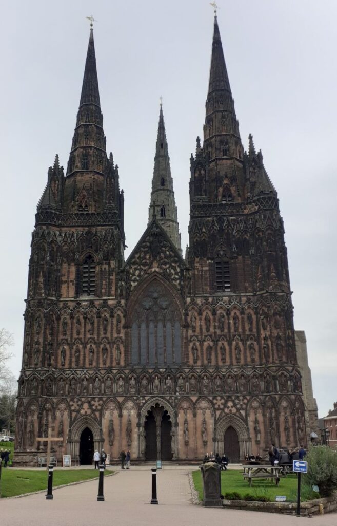 The front of Lichfield Cathedral with a few people standing around it.